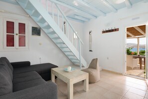 A room with a staircase, a sofa, a table with a cup, a chair, and a view of the sea. - House with stunning sea views in Agios Sostis (Μύκονος)