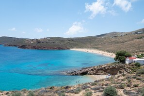 A coastal landscape with a beach, rocky terrain, and a few buildings. - House with stunning sea views in Agios Sostis (Μύκονος)