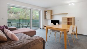 A modern room with a sofa, a dining table with chairs, a built-in wooden cabinet, and a sliding glass door leading to an outdoor area. - Apartment 'Talferblick Burg' with Mountain View, Private Terrace and Wi-Fi (Sarentino)