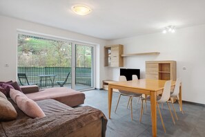 Une pièce moderne comprenant un canapé, une table à manger avec des chaises, un meuble encastré en bois et une porte-fenêtre coulissante donnant sur un espace extérieur.