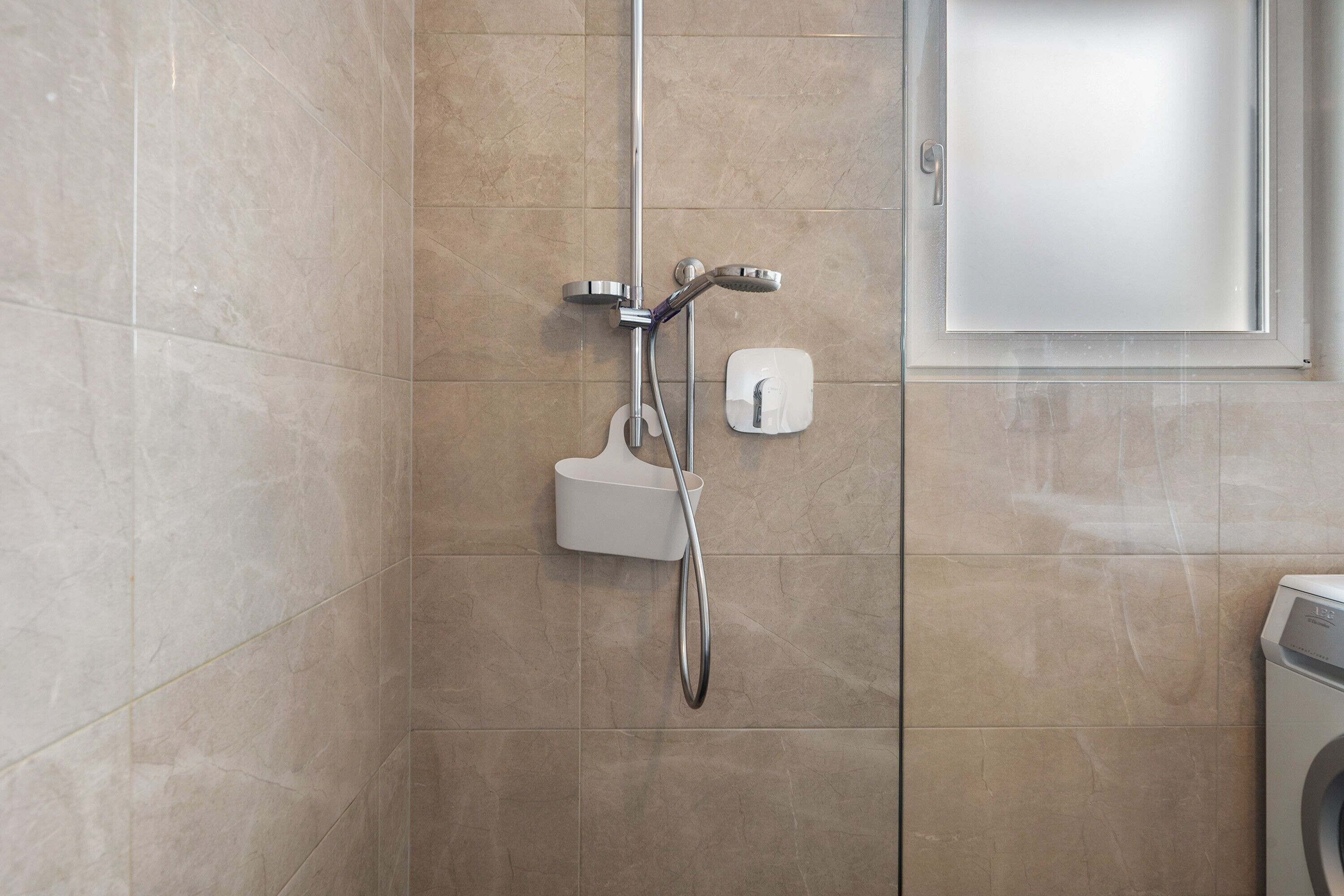 Een badkamer met een douche, toilet en een wasmachine.