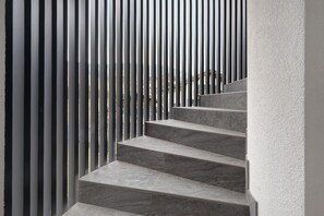 Un conjunto de escalones de mármol gris que suben a una plataforma, rodeados de listones metálicos verticales.