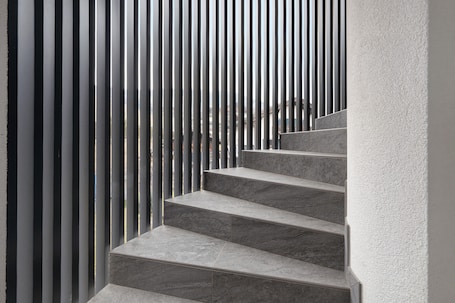 A set of grey marble stairs leading up to a landing, surrounded by vertical metal slats.