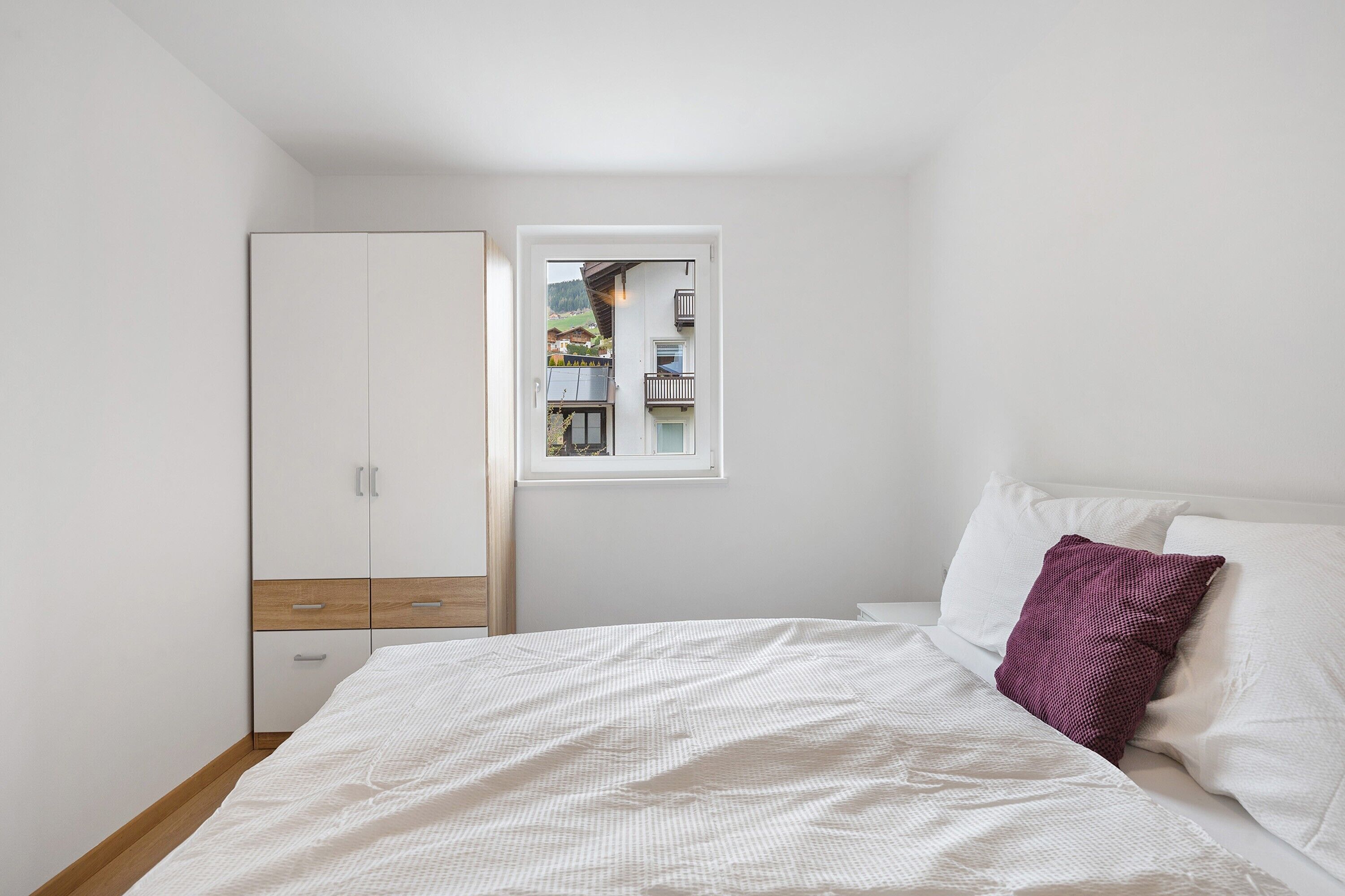 Une chambre à coucher avec un lit, des murs blancs, une armoire et une fenêtre donnant sur un balcon.