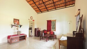 A spacious living room with a high ceiling, a sofa, a coffee table, a wooden cabinet, and a dining table. - Arokiya (Shoolagiri)