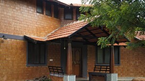 A brick building with a covered porch, a wooden door, and two benches. - Laze Daze (Shoolagiri)