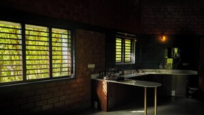 A modern kitchen with a central island, large windows with blinds, and a brick wall. - Laze Daze (Shoolagiri)