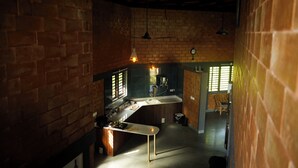 A kitchen with a brick wall, a countertop, and hanging pendant lights. - Laze Daze (Shoolagiri)