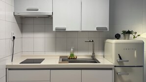 A modern kitchen with white cabinets, a built-in sink, a stainless steel faucet, a small refrigerator, and a light under-cabinet. - JS Building-503 (Seoul)