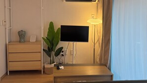 A modern room with a flat-screen TV, a bedside lamp, a potted plant, and a wooden dresser. - JS Building-503 (Seoul)