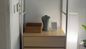 A compact room with a wooden cabinet, a wicker basket, a decorative vase, a framed mirror, and a tall white lamp. - JS Building-503 (Seoul)