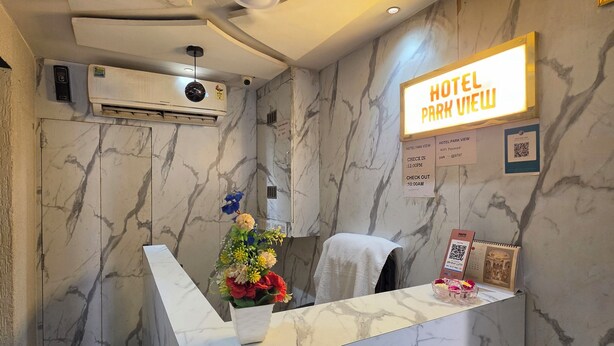 A hotel reception desk with a marble design, a 'Hotel Park View' sign, and a reception area with a flower arrangement. - Hotal Park View (Ahmedabad)