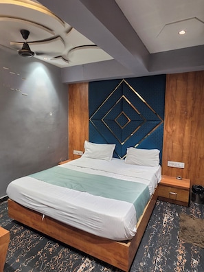 Une chambre d’hôtel moderne avec un lit, une tête de lit en bois et un ventilateur de plafond.