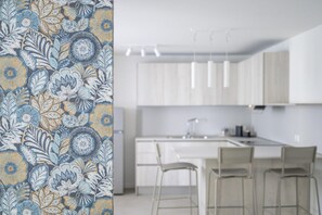 A modern kitchen with white cabinets, a central island with bar stools, and pendant lighting. - Elegant Apartment for Unforgettable Stays (San Michele al Tagliamento)