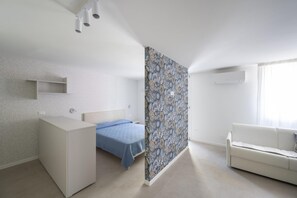 A bedroom with a bed, a white dresser, a white sofa, a patterned wall, and a ceiling light fixture. - Elegant Apartment for Unforgettable Stays (San Michele al Tagliamento)
