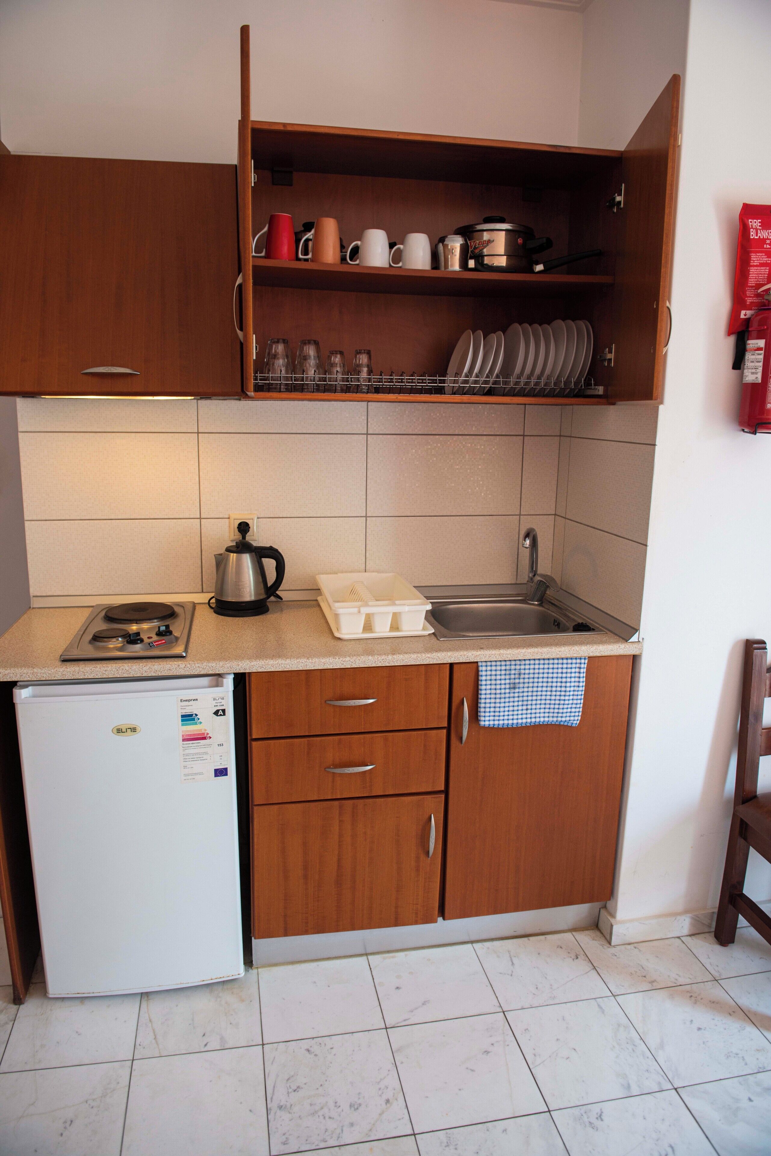 A compact kitchen with a refrigerator, stove, sink, and wooden cabinets.