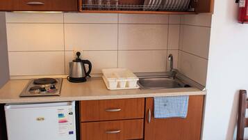 A compact kitchen with a refrigerator, stove, sink, and wooden cabinets.