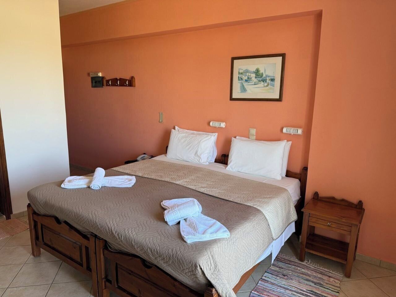 A neatly made bed with a brown quilt, white pillows, and two rolled towels on the bed.