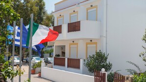 A two-story building with balconies, a flag, and a clear sky. - Luis Pool (Kos)