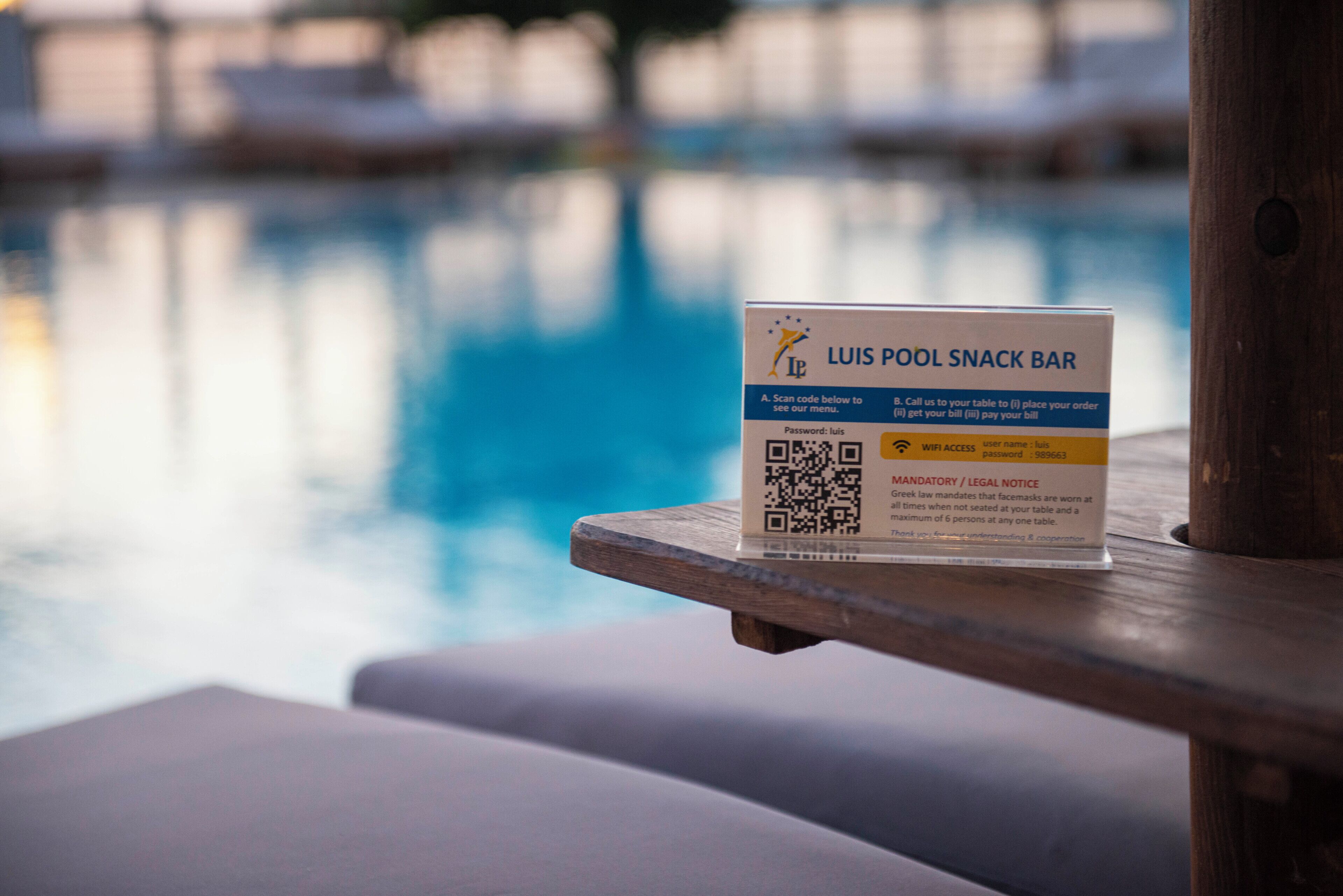 A poolside sign for Luis Pool Snack Bar with a QR code and WiFi access information.