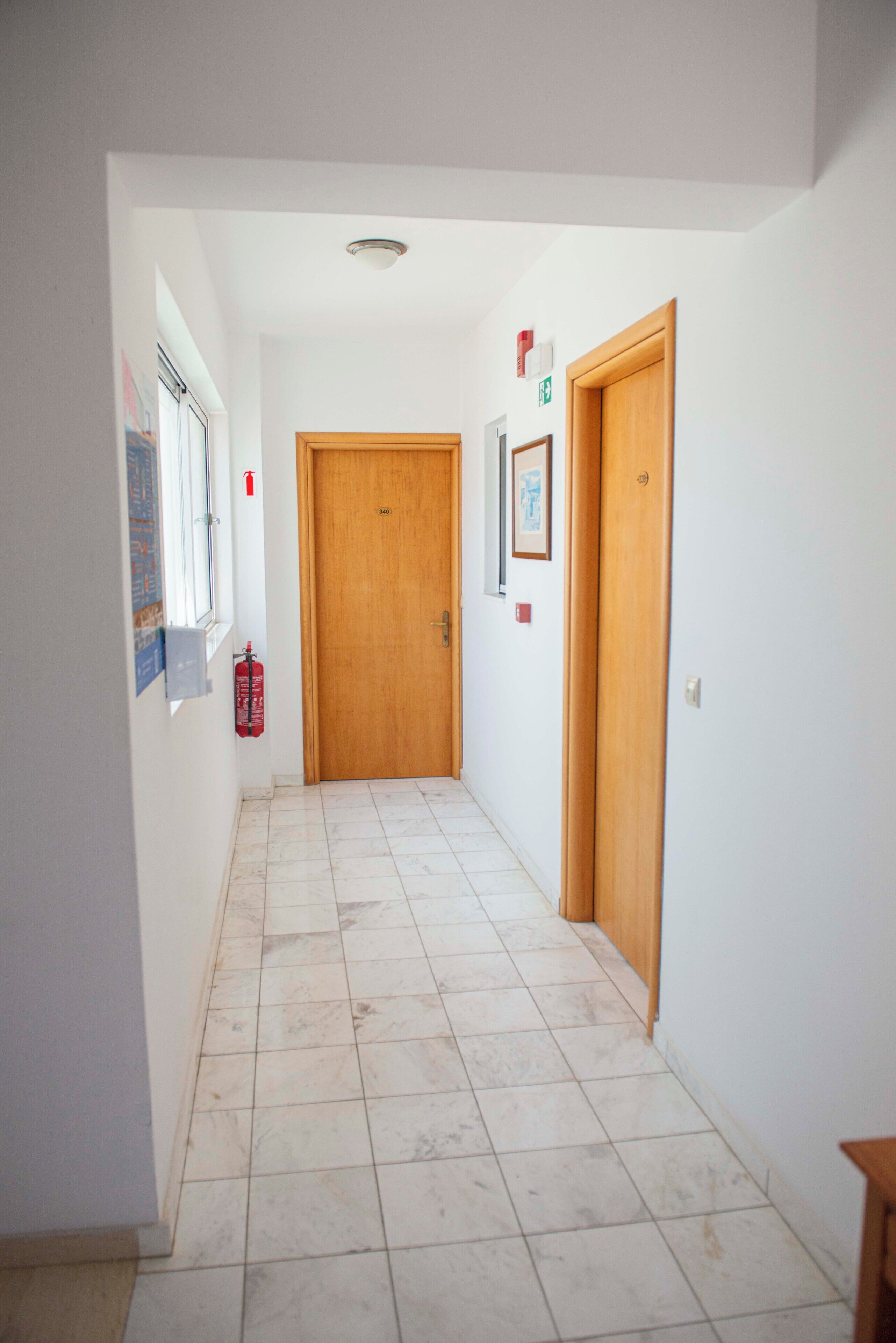 A hallway with tiled flooring, wooden doors, and a fire extinguisher on the wall.