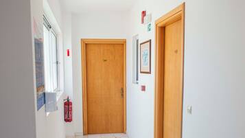 A hallway with tiled flooring, wooden doors, and a fire extinguisher on the wall.