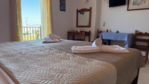 A hotel room with two beds, a TV, a table with a checkered tablecloth, and a balcony view. - Luis Pool (Kos)