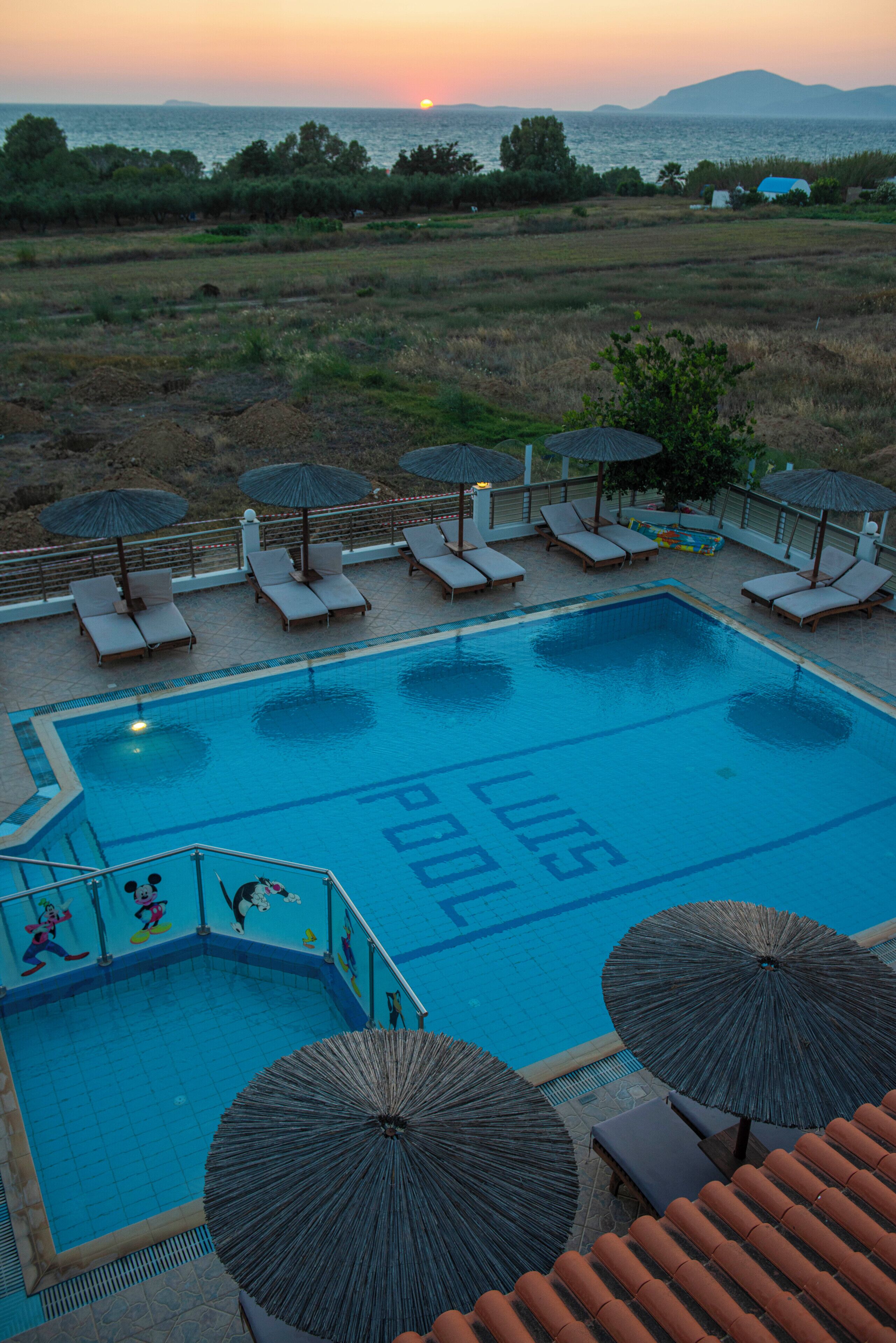 A swimming pool with lounge chairs and umbrellas, surrounded by a landscaped area with a view of the sea and hills.