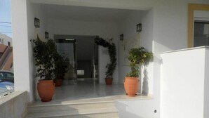 A building entrance with steps, potted plants, and a glass door. - Luis Pool (Kos)