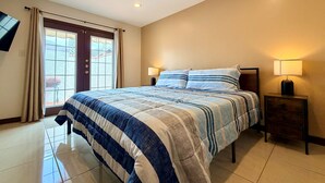 Habitación de hotel con cama, dos mesitas de noche, televisor montado en la pared y ventana con cortinas.