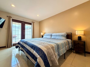 A hotel room with a bed, two bedside tables, a TV mounted on the wall, and a window with curtains.