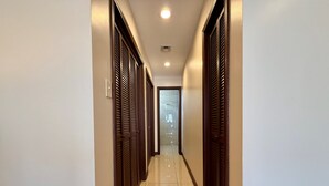 Un pasillo con puertas de madera, piso de baldosas y una lámpara en el techo.