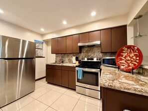 A modern kitchen with stainless steel appliances, granite countertops, and brown cabinetry.