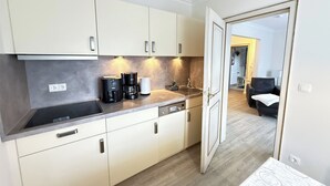 A modern kitchen with a coffee maker, a toaster, and a sink. There is a door leading to a living area with a sofa and a lamp. - Vacation apartment Um's Eck in Haus Inselfriede very close to the beach in Westerland (Westerland)