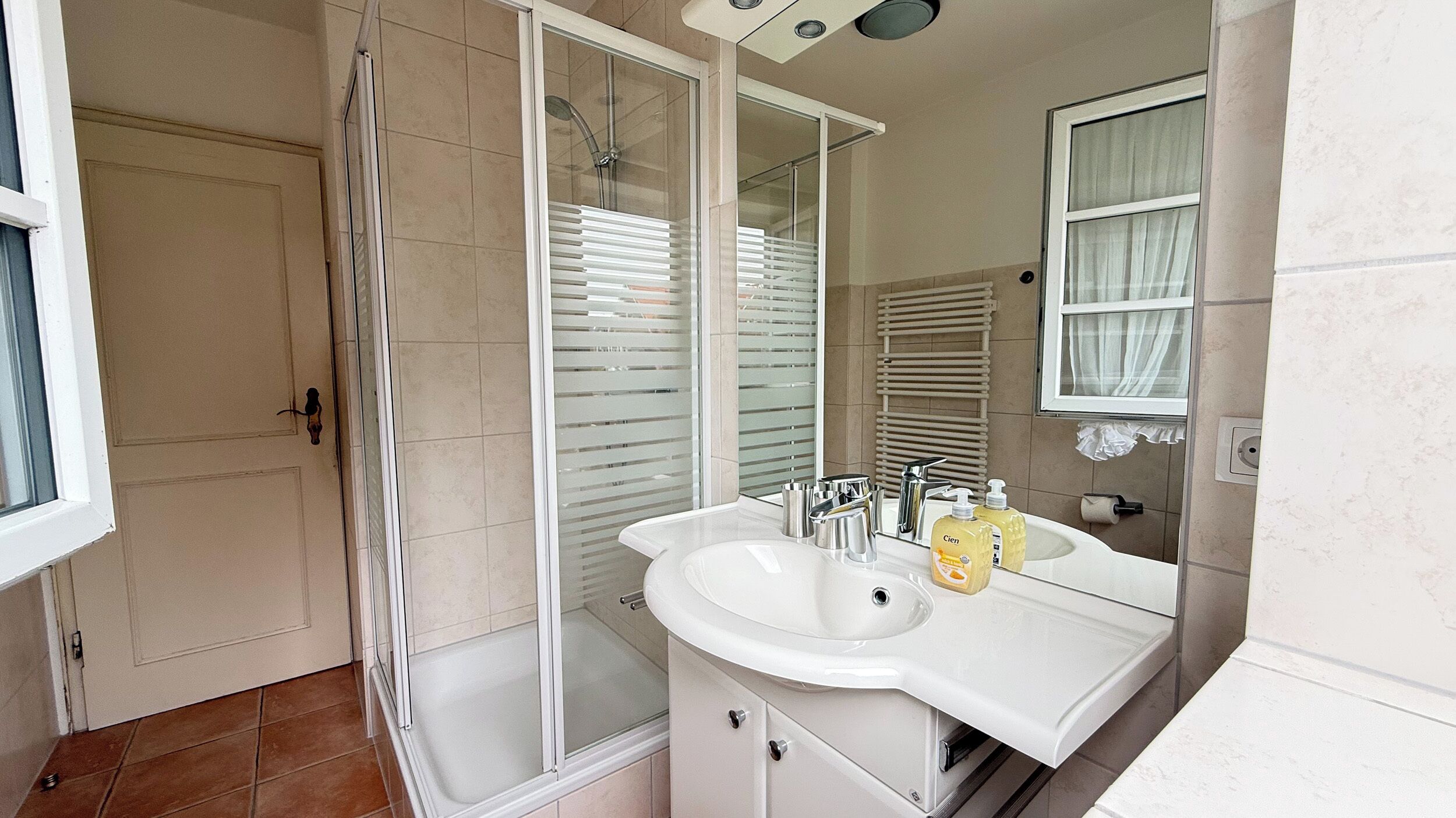 A bathroom with a glass shower enclosure, a white sink with a mirror, and a towel rack.