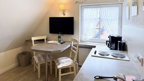 Pieni keittiö, jossa on ruokapöytä, tuoleja, televisio, ikkuna, jossa on verhot, ja patteri.