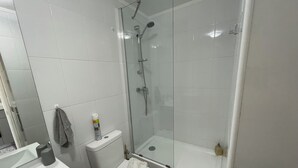 Un baño con ducha de vidrio, inodoro y lavamanos.