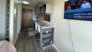 Una cocina moderna con horno empotrado, microondas y pileta. Hay un televisor en la pared que muestra un noticiero.