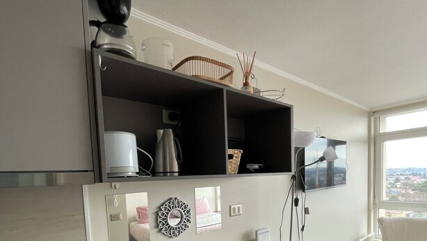 Una cocina moderna con una encimera larga, una cafetera, un hervidor y un microondas. Hay un comedor con una mesa y sillas, y una ventana con vistas a la ciudad.