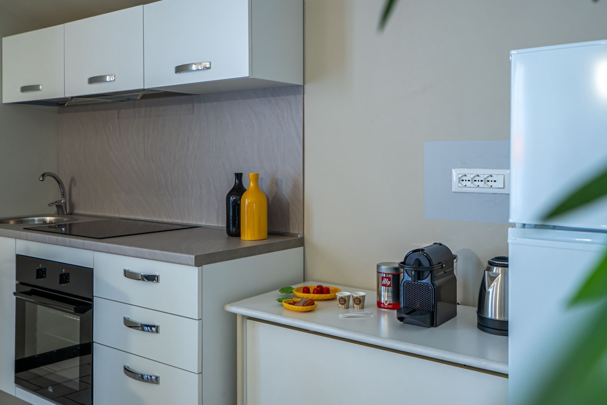 A modern kitchen with white cabinets, a stainless steel sink, a built-in oven, and a white refrigerator.