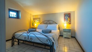 Un dormitorio con una cama, dos mesitas de noche, un ventanal y dos lámparas de pared.