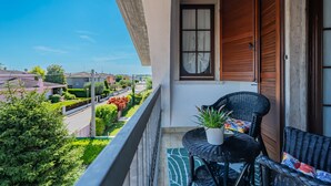 Un balcón con mobiliario de mimbre, una planta en maceta y vistas a un barrio residencial.
