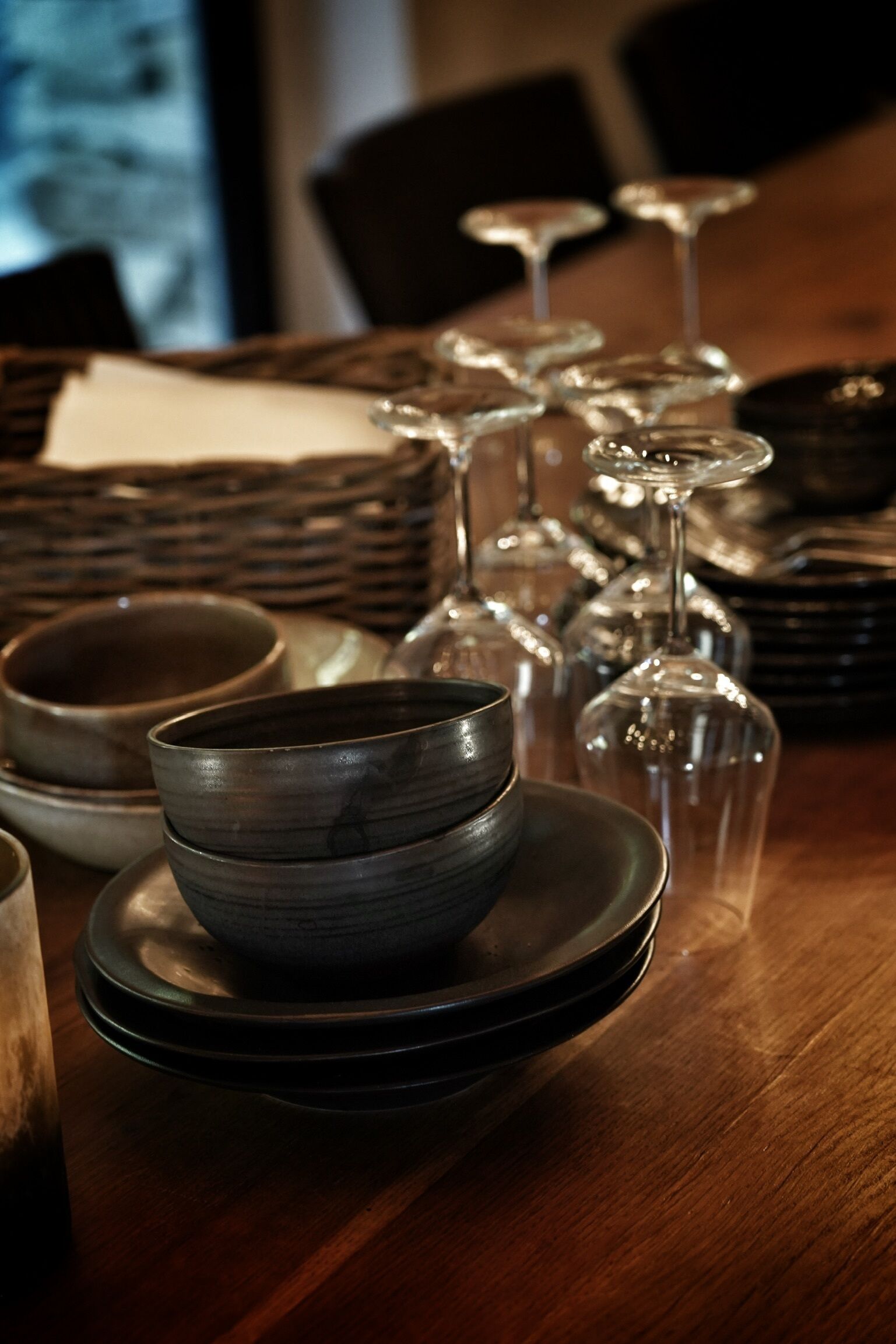 A dining table with stacked plates, bowls, and wine glasses.