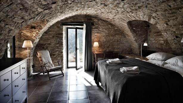A stone-walled bedroom with a bed, a chair, a dresser, and a lamp. - Villa dell’Orso – Secluded Luxury with Private Infinity Pool & Piedmont Views (Piemonte)