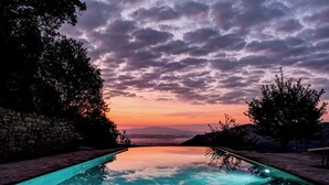 A swimming pool with a stone wall on one side and trees on the other, set against a sunset sky. - Villa dell’Orso – Secluded Luxury with Private Infinity Pool & Piedmont Views (Piemonte)