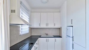 Eine kleine Küche mit weißen Schränken, einer schwarzen Arbeitsplatte, einem Einbauofen und einem K ühlschrank.