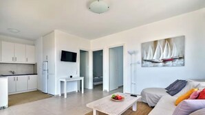 Ein modernes Wohnzimmer mit einer Couch, einem Couchtisch mit Obst, einem Flachbildfernseher und einem Segelbootgemälde an der Wand.