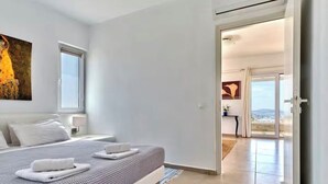 Ein modernes Schlafzimmer mit einem großen Bett, einem Gemälde an der Wand und Blick durch eine offene Tür auf einen Balkon.