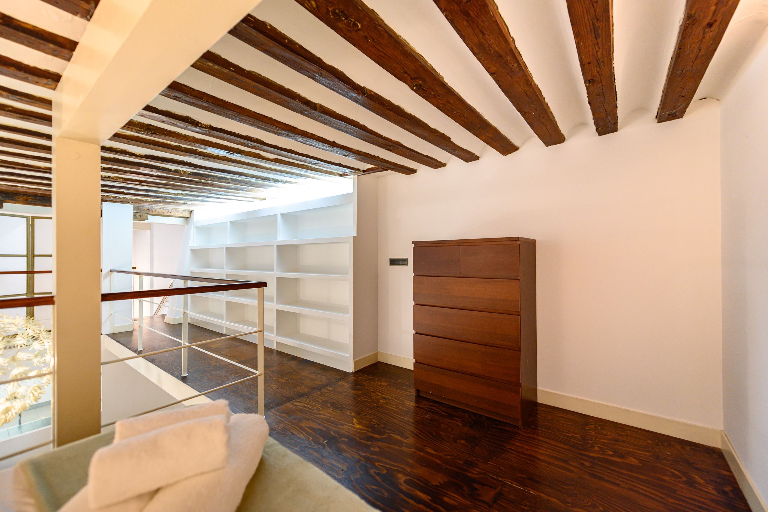 Un interior moderno con techo de madera, baranda de cristal y estantería empotrada.