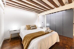 A bedroom with a bed, bedside tables, a wardrobe, and a ceiling with wooden beams. - (ESA121ID) Spacious Duplex in the center of Madrid (Madrid)